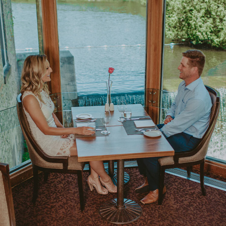 A couple dining in Headwaters Restaurants beside Shaw’s Creek Falls at Millcroft Inn & Spa.